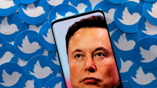 An image of Elon Musk is seen on a smartphone placed on printed Twitter logos