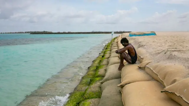 A man sits on a protective sand bag wall on October 10, 2021 in Guraidhoo, Maldives