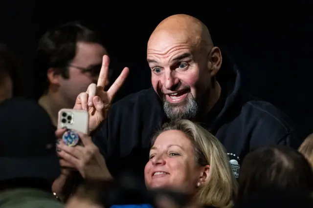 Democratic Senate candidate for Pennsylvania John Fetterman holds two fingers up in a 'peace' sign as a supporter takes a selfie with him