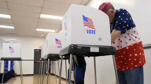 A man in a starry red, white and blue top votes at a polling booth