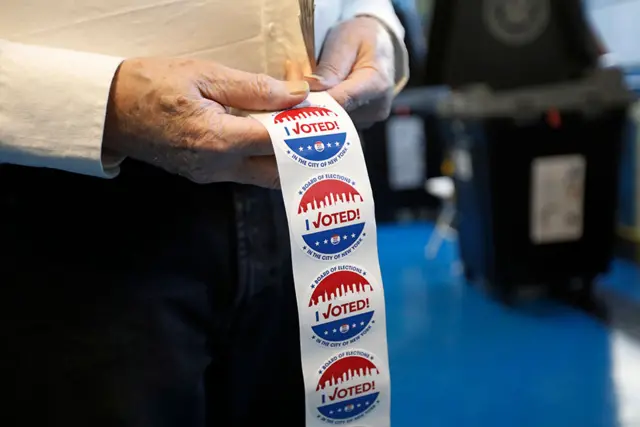 A poll worker with a roll of 'I Voted' stickers at Public School 111 in New York, New York, USA