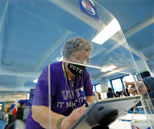 A poll worker in a mask face mask with 'vote' written in diamantes on it assists voters at Public School 111 in New York, US, on 8 November