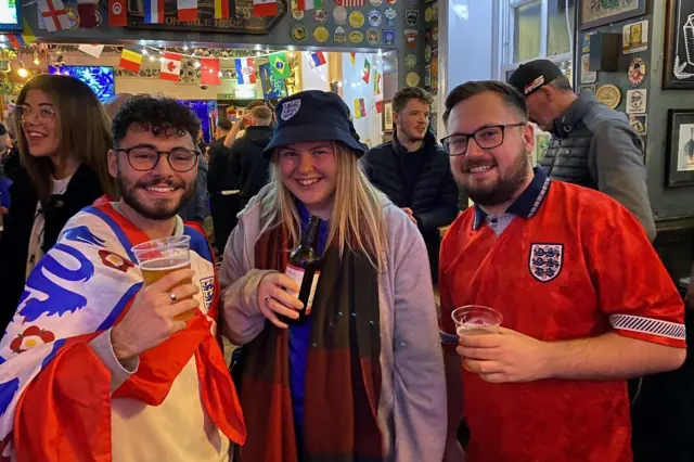 Three England fans holding drinks pose for a photo in a pub