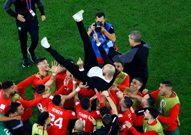 Morocco players throw coach Walid Regragui in the air as they celebrate qualifying for the quarter finals