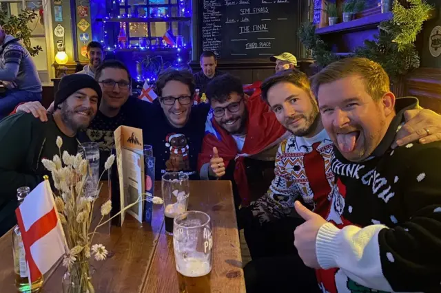 Six England football fans are pictured wearing Christmas jumpers in a pub