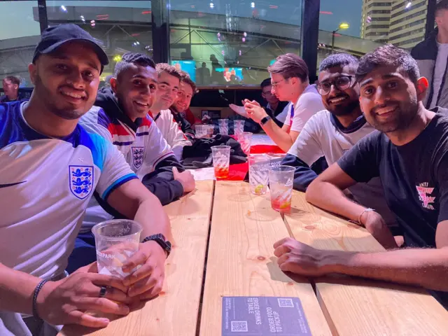 Fans wearing England shirts sit around a table having drinks