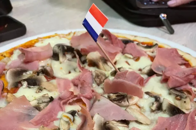 A ham and mushroom pizza with a French flag stuck in it