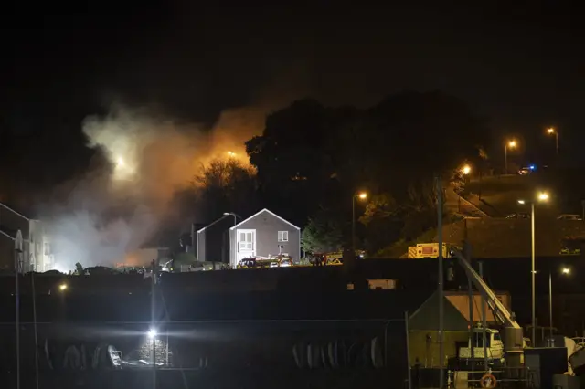 Grey smoke billows from where a building was at nighttime