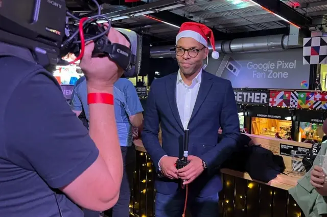 BBC London's Greg McKenzie wears a Father Christmas hat in front of a camera