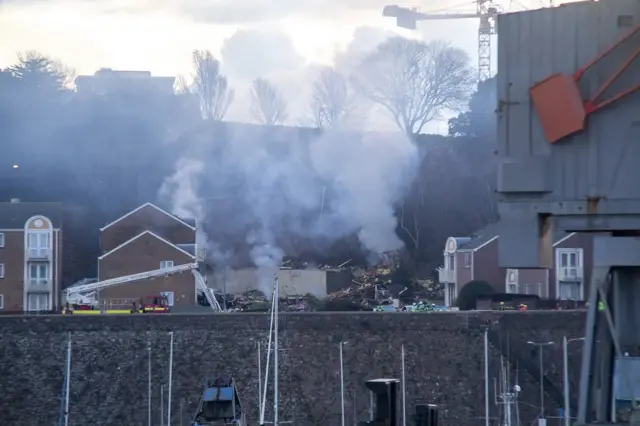 Smoke billows from debris in the ground where a building once stood