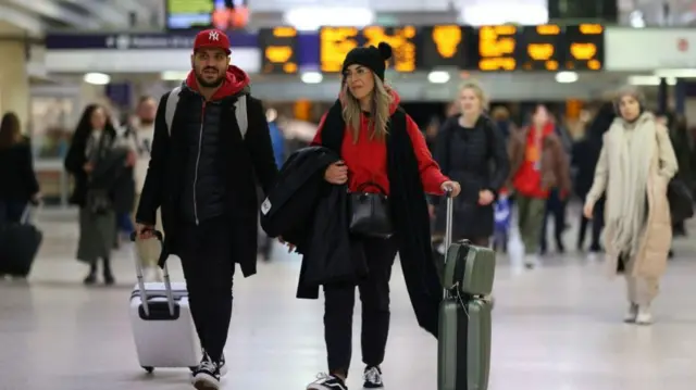 People walk with suitcases through a train station