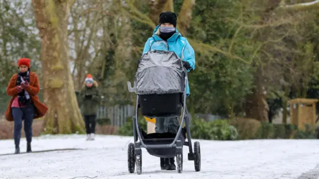 A woman with a baby pram braves the snow and freezing temperatures in north London
