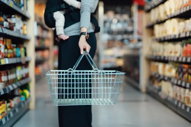 A woman carries a shopping basket in a supermarket