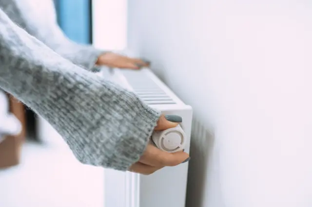 Woman turning down thermostat on radiator