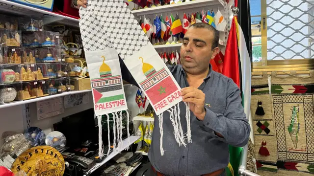 Gaza City flag-supplier Tareq Abu Dayyeh holds up a keffiyeh bearing the Palestinian and Moroccan flags