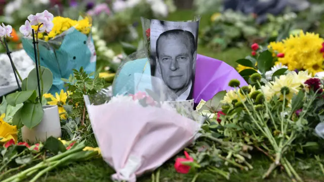 A photograph of Britain's Prince Philip, Duke of Edinburgh is positioned among floral tributes outside Windsor Castle in Windsor, west of London, on April 10, 2021, the day after the duke's death at the age of 99