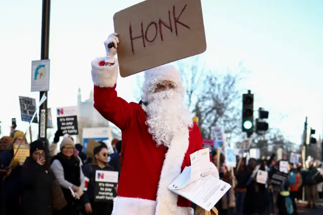 A demonstrator dressed as Santa shows a "HONK" sign at drivers as NHS nurses strike, amid a dispute with the government over pay, outside St Thomas' Hospital in London