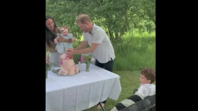 Archie sits and watches his parents and sister during a birthday party