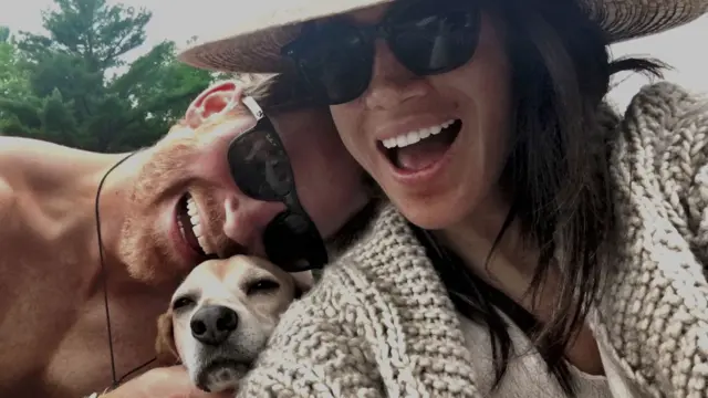 Harry and Meghan smiling in a selfie, with a dog also in the picture