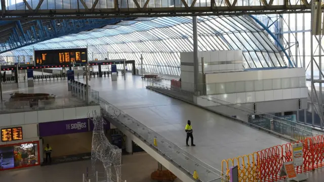 A station employee stands on a closed section of a deserted concourse at London Waterloo