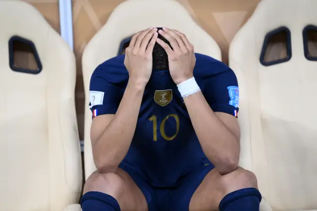 Kylian Mbappe sits on the France bench with his face covered by his shirt