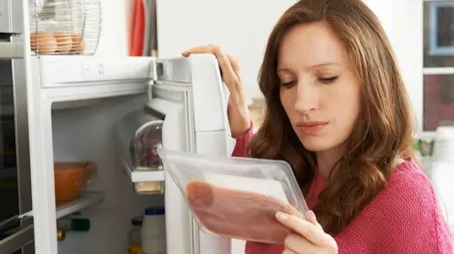 Stock image of woman checking a refrigerated product's use-by date