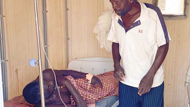 A man standing by William Mponda's bed at Lisungwi community hospital, Malawi