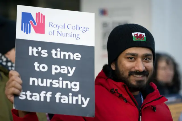 A man in a hat with the Welsh dragon on it holds a placard