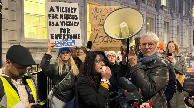 Protesters hold placards and a woman speaks into a megaphone outside Downing Street