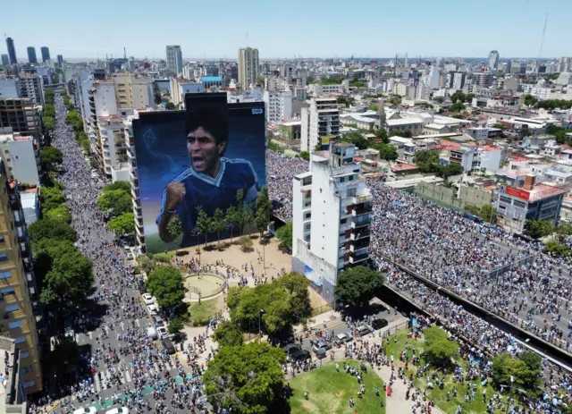 A mural of Diego Maradona is seen with Argentina fans during the victory parade