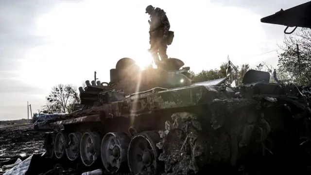 A Ukrainian serviceman surveys a destroyed Russian tank