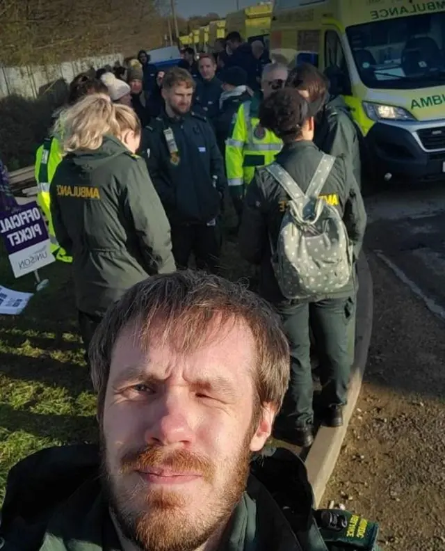 Arron Glenwright-Cook selfie with striking paramedics in the background