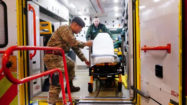 A man in military uniform helps an ambulance worker at the back of an ambulance