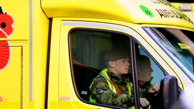 A person in military uniform and a hi-vis vest drives an ambulance