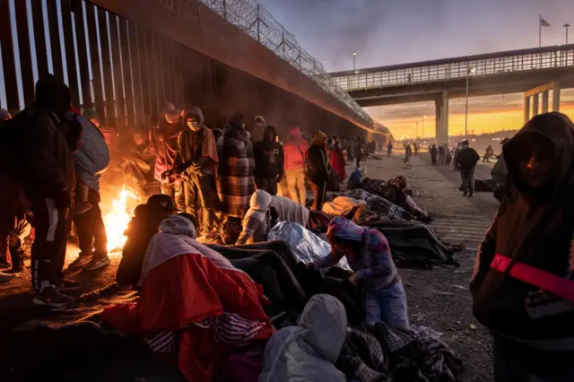 Migrants warn themselves around a fire on the streets of El Paso, Texas