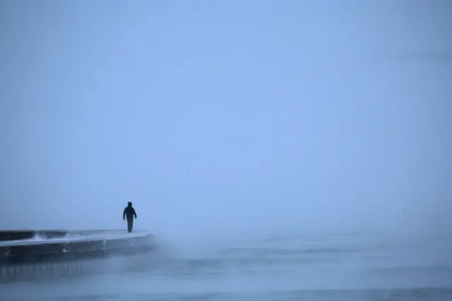 A man walks along a misty Lake Michigan at sunrise