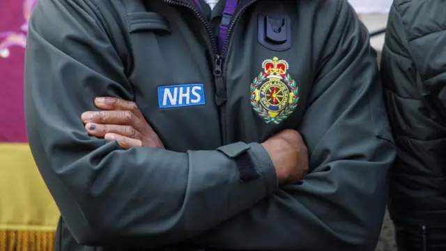 A close-up of an ambulance worker shown with their arms folded, their face out of shot