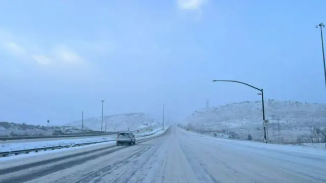 A snow covered road with one car seen ahead