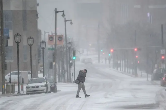 A person walks across a road in snow.