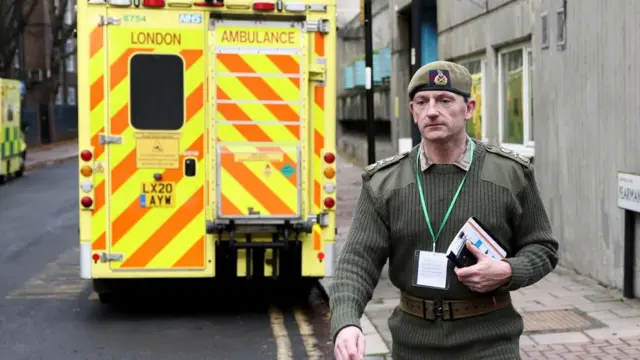 A member of the military walks in front of an ambulance