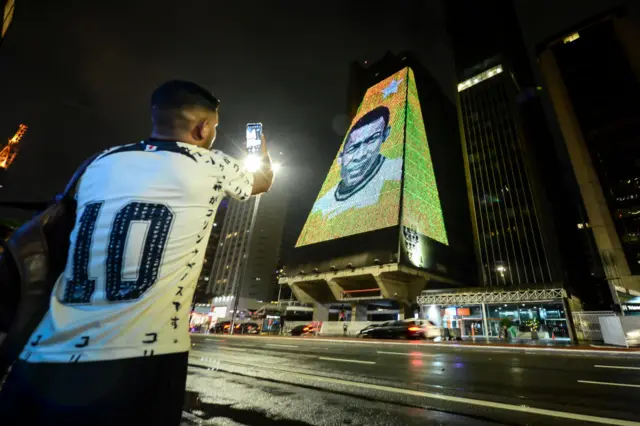 A man takes photos of an image of Pele displayed on a building in Sao Paulo, Brazil