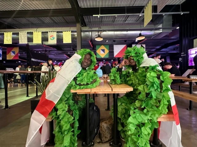 Two men dressed as trees wearing England flags draped around their necks, sat at a table in Wembley Box Park