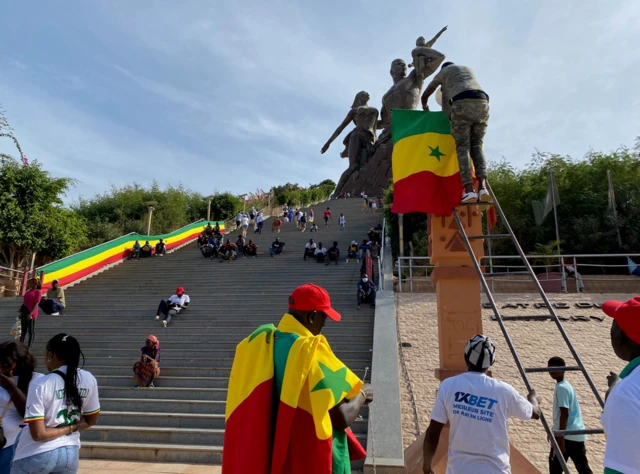 Fans carrying Senegal flags gather in front of the steps leading up to of a Dakar’s African Renaissance monument