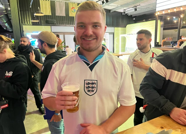 Luke Benton on and England shirt holding a pint of beer