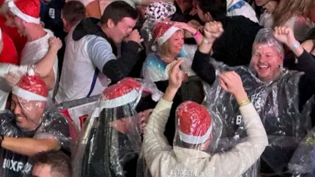 England fans celebrating after the goal, several wearing santa hats and plastic ponchos