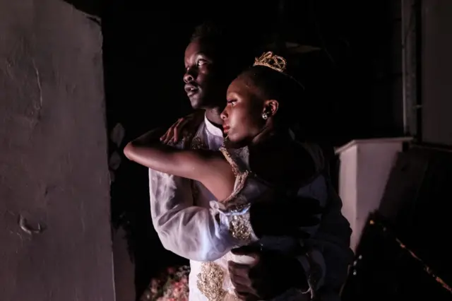 A young man and woman perform in a ballet. They are at the side of the stage waiting to go on.