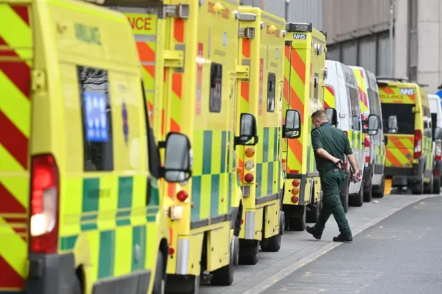 An ambulance worker walks among a long line of parked ambulances