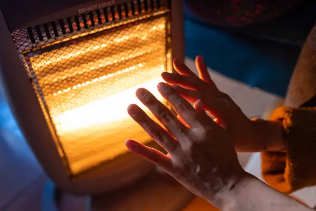 A woman warms her hands on an electric heater