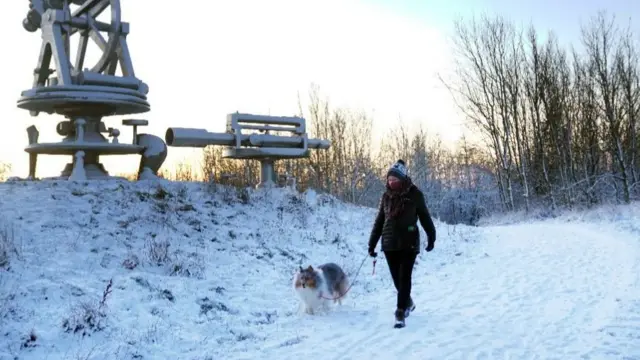 A woman walks her dog through snow near the Terris Novalis sculpture in Consett, County Durham.