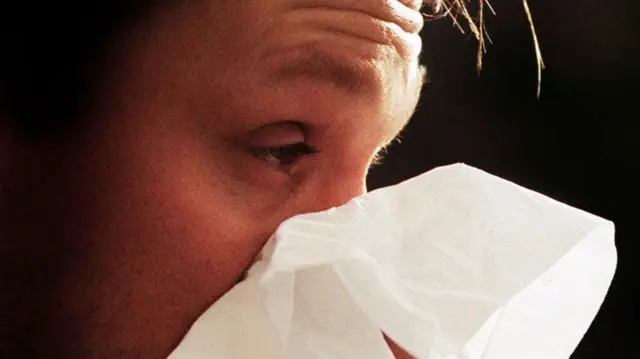 A man sneezes into a tissue